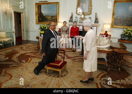 Königin Elizabeth II. Verleiht dem neuseeländischen Generalgouverneur Anand Satyanand die Auszeichnung zum Rittertum, während seine Frau Susan und seine Tochter Tara im Buckingham Palace im Zentrum von London auf sie blicken. Stockfoto