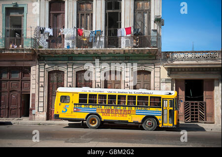 gelber Schulbus unter Wäscheleine mit Kleidung zum Trocknen aufhängen Stockfoto