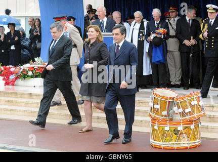 Premierminister Gordon Brown, Frau Sarah und der französische Premierminister Francois Fillon verlassen die Bühne, um sich bei einem Gedenkgottesdienst in Arromanche, zum 65. Jahrestag der Landung in der Normandie, mit Veteranen zu mischen. Stockfoto