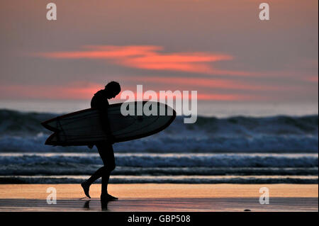 Ein surfer Spaziergänge am Strand bei Sonnenuntergang Stockfoto