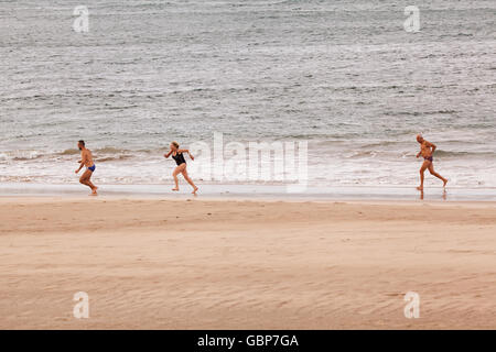 Drei Personen mittleren Alters, zwei Männer und eine Frau, die entlang des Strandes beim Schwimmen tragen Stockfoto