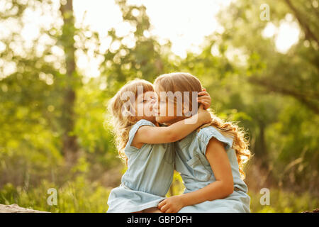 Zwei niedliche kleine Schwestern umarmen in einem Park an einem sonnigen Sommertag. Jüngere Schwester küssen elder. Zeit mit der Familie. Stockfoto