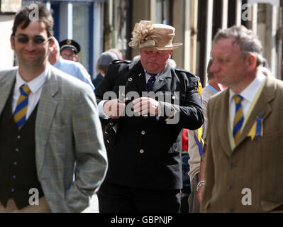 Ein Mitglied der Hawick Fifes and Drums Band kommt in den Partygeist, indem es im Hawick Common Riding auf der Hawick High Street einen Frauenhut trägt. Stockfoto