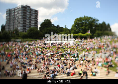 Am 3. Tag der Wimbledon Championships 2009 im All England Lawn Tennis and Croquet Club, Wimbledon, London, versammeln sich Massen auf einer Bank, um den großen Fernsehbildschirm zu sehen. Stockfoto