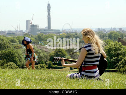 Ein Mädchen spielt Gitarre, während die Menschen die Sonne auf Primrose Hill, London genießen. Stockfoto