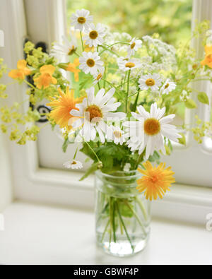 Jam Jar Blumen - ziemlich informelle Abmachung von gelben und weißen Sommer Wildblumen auf Küche Fensterbank in Großbritannien Stockfoto