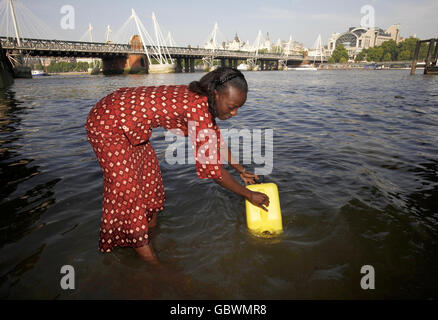 Eine Afrikanerin in traditioneller Kleidung füllt eine jerry-Dose mit Wasser aus der Themse, um sie in die Downing Street in London zu bringen, wo sie - zusammen mit anderen afrikanischen und asiatischen Frauen - 80,000 Briefe der britischen Öffentlichkeit einreichen wird, Im Namen der Kampagne „Ende der Wasserarmut“. Stockfoto