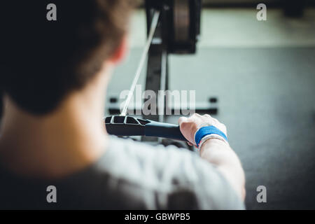 DER JUNGE Mann in den Zwanzigern, der sich auf der Rudermaschine aufwärmte. Stockfoto