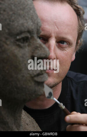 Der Künstler Daniel Doyle setzt die Oberflächen seiner lebensgroßen Sandskulptur mit zwei Sandtönen. Die Skulptur zeigt die menschlichen Auswirkungen des Klimawandels während der Oxfam Ireland Kampagne von Climate Change Destroy's Lives - Let face it Kampagne in Dublin. Stockfoto