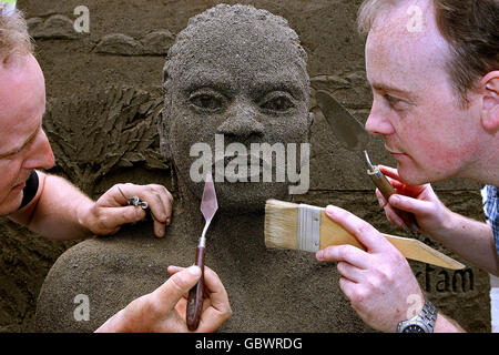 Der Künstler Daniel Doyle (links) und sein Neffe Nathaniel setzen die Oberflächen berührt seine lebensgroße Sandskulptur mit zwei Sandtönen. Die Skulptur zeigt die menschlichen Auswirkungen des Klimawandels während der Oxfam Ireland Kampagne von Climate Change Destroy's Lives - Let face it Kampagne in Dublin. Stockfoto