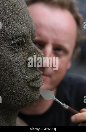 Der Künstler Daniel Doyle setzt die Oberflächen seiner lebensgroßen Sandskulptur mit zwei Sandtönen. Die Skulptur zeigt die menschlichen Auswirkungen des Klimawandels während der Oxfam Ireland Kampagne von Climate Change Destroy's Lives - Let face it Kampagne in Dublin. Stockfoto