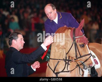 HRH der Prinz von Wales setzt eine Rosette auf den Gewinner des Weihnachtspakes Virtual Village Grannusch, wie Reiter John Whitaker anschaut Stockfoto