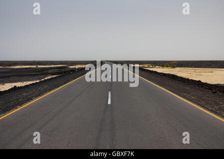 Eine leere Autobahn, die auf vulkanischem Gestein gebaut wurde, erstreckt sich über die Danakil-Depression in Äthiopien in Richtung der Grenze zu Dschibuti Stockfoto