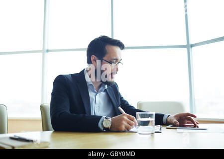 Ernsthaften Geschäftsmann arbeiten mit Touchpad und Notizen im Dokument Stockfoto
