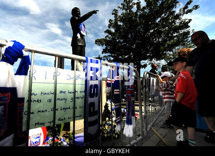 Zwei Jungen sehen zu, wie neben einer Statue von Bobby Robson vor dem Fußballverein von Ipswich Town Ehrungen zu sehen sind, in Erinnerung an den Fußballmanager, der heute verstorben ist, Ipswich. Stockfoto