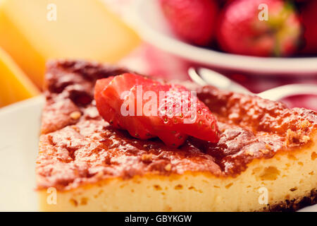 Nahaufnahme einer Platte mit einem Stück hausgemachter Käsekuchen garniert mit in Scheiben geschnittenen Erdbeeren auf einem gedeckten Tisch Stockfoto