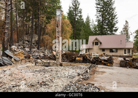 Ruinen eines Hauses, das auf den Boden verbrannt, während benachbarte Haus nach einer Naturkatastrophe Wald intakt bleibt Feuer Lauffeuer Stockfoto
