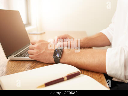 Schließen Sie herauf Bild der Geschäftsmann am Laptop arbeiten. Mann mit einer Smartwatch mit Laptop-Computer während der sitzt an seinem Schreibtisch. Stockfoto