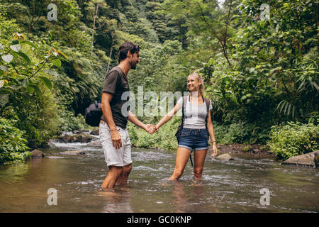 Liebevolle junge Paar in Waldbach stehen. Junger Mann und Frau im Fluss, die Hand in Hand. Spaß auf Wandertag. Stockfoto