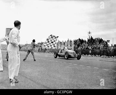 Der britische Rennfahrer Reg Parnell, der einen Maserati 4CL fährt, hebt seine Hand zum Feiern, als er die Zielflagge nimmt. Stockfoto