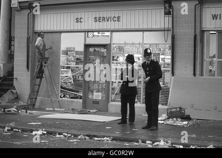 Die Polizei steht Wache, als ein Arbeiter an diesem Morgen ein Fenster des Co-Op Supermarket und aus Lizenz in Westbourne Park Road nach den gewalttätigen Szenen gestern Abend auf dem Notting Hill Karneval begibt. Stockfoto