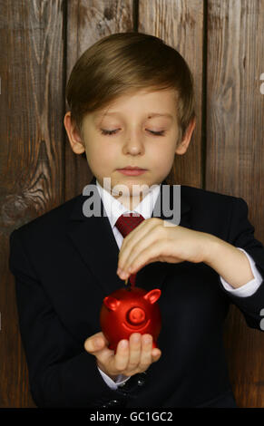 Junge in einem Anzug mit einem roten Sparschwein - Business-Konzept Stockfoto