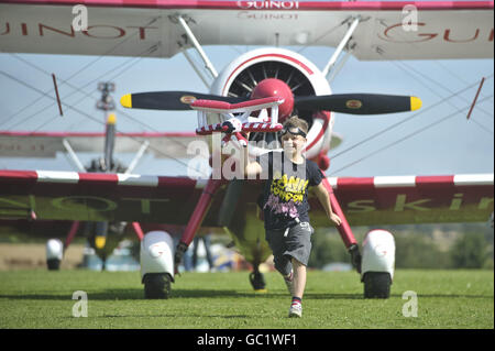 Der achtjährige Tiger Brewer spielt mit einem aufblasbaren Doppeldecker, während er vor dem eigentlichen Doppeldecker-Flugzeug sitzt, mit dem er herumlief und der jüngste Flügelgänger der Welt auf dem RFC Rendcomb Airfield in der Nähe von Cirencester wurde. Stockfoto