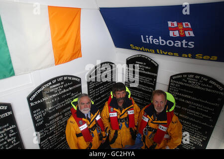 Besatzungsmitglieder des Howth RNLI Rettungsbootes (links nach rechts) Rupert Jeffares, Robert Duffy und George Duffy, stehen unter der Aufmerksamkeit neben kommerziellen Plaketten im Bootshaus am Howth Pier, Dublin, Als RNLI in Großbritannien und Irland ehren und erinnern sich Besatzungsmitglieder, die im Dienst umkamen. Stockfoto