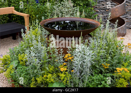 Naturalistische Pflanzen rund um eine Runde Metall Wasserspiel im A Sommergarten Retreat an der Hampton Court Palace Flower Show Stockfoto