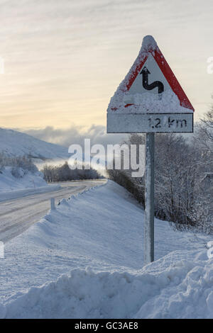 Winterliche Straße mit Warnschild, Europastraße E10, kurvenreichen Strecke, Insel Hinnøya, Nordland, Norwegen Stockfoto