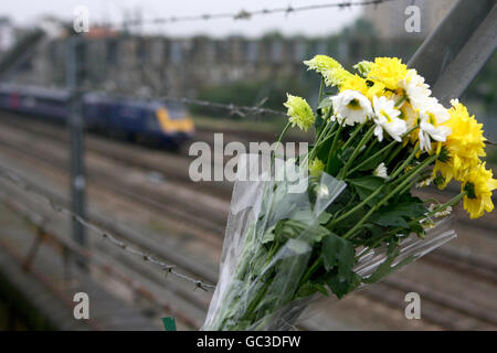 Ein erster Great Western-Zug nähert sich London (hinter dem Zug gesehen), als Blumen von Überlebenden und trauernden Familien hinterlassen werden, die zum 10. Jahrestag des Eisenbahnunglücks in Paddington in Ladbroke Grove im Westen Londons kamen. Stockfoto