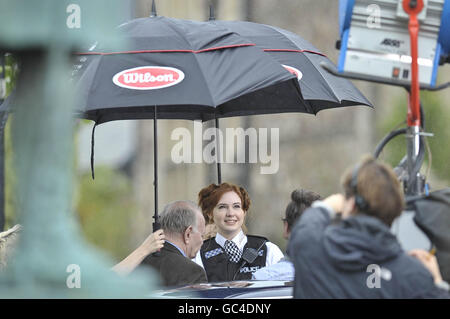 Die Assistentin des Doktors, die Schauspielerin Karen Gillan, als Polizeibeamter gekleidet, wird während der Dreharbeiten in der Nähe der Kathedrale in Llandaff, Cardiff, Wales, vor dem Regen geschützt, wo die neueste Serie von Doctor Who gedreht wird. Stockfoto