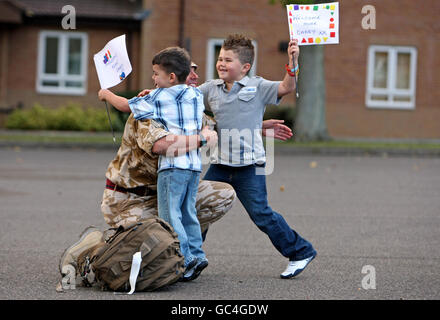 Stabsfeldwebel Kevin Vaughan wird von seinen Söhnen Owen, fünf, links, und Bradley, 6, Als 75 Royal Engineer und Royal Logistic Corps nach sechs Monaten in Afghanistan Bombenentsorgungs- und Suchspezialisten nach Carver Barracks, Wimbish, Essex zurückkehren. Stockfoto