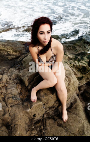 Hispanische Frau sitzen auf den Felsen mit Meerwasser hinter ihr mit einem Bikini von oben gesehen Stockfoto
