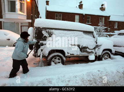 Eine Frau räumt in St. Boswells an der schottischen Grenze nach einer Nacht mit starkem Schneefall Schnee aus ihrem Auto. Stockfoto