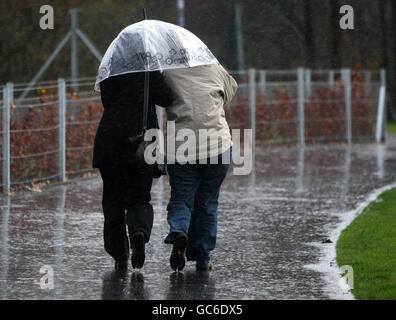 Zwei Menschen schützen sich vor dem West Lothian Civic Center in Livingston unter demselben Regenschirm vor Regen und Wind. Stockfoto