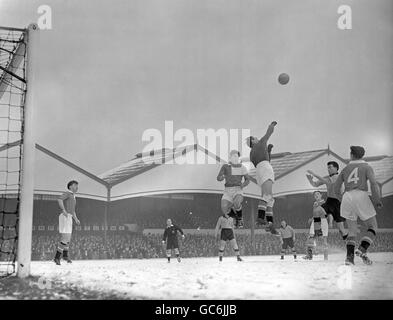 Manchester United Torwart Ray Wood und Teamkollege Duncan Edwards, Mitte, springen hoch über dem schneebedeckten Spielfeld, um einen Freiraum von einem Wolves Angriff zu machen, angeführt von Center Forward Jimmy Murray (Arme nach vorne). Links sieht man Bobby Charlton von Manchester United. Stockfoto