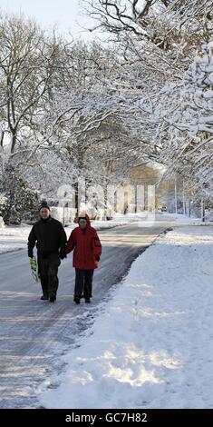 Ein paar Spaziergang entlang einer eisbedeckten Straße in Stock Village, Essex, nach schweren Schneefällen in der Grafschaft. Stockfoto