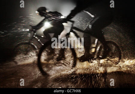 Zwei Mountainbiker machen sich mit nur einer Fackel auf eine Fahrt in der Nacht, um sich über Felsen und Wälder auf einem der beliebtesten Mountainbike-Strecken Schottlands, Glentress, in den Scottish Borders, über schwere Hügel zu entflammen. Stockfoto