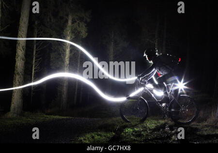 Ian Grant einer der Mountainbiker macht sich auf eine Fahrt bei nasser Nacht mit nur einer Fackel auf, um sich auf einem der beliebtesten Mountainbike-Strecken Schottlands, Glentress, in den Scottish Borders, über Felsen und durch Wälder hinabzusetzen. Stockfoto