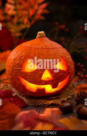 Brennen von Jack O'Lantern auf einem rustikalen Tisch mit herbstlichen Dekorationen, beleuchtet dunkel. Stockfoto