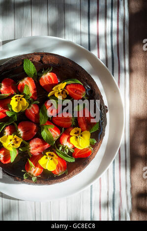 Schokoladenkuchen mit Erdbeeren und Eddible Blumen in einem Garten Stockfoto