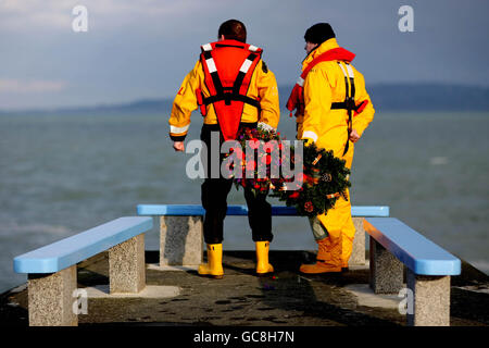 Harry McLoughlin und Kieran O Connor, Crew-Mitglieder der RNLI-Rettungsstation Dun Laoghaire, blicken bei einer Zeremonie am östlichen Pier von Dun Laoghaire mit Kränzen auf das Meer, um gefallene Kollegen zu ehren, die am Heiligabend des Jahres 1895 ihr Leben auf See verloren haben. Stockfoto