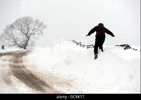 Ein Fußgänger geht entlang einer Straße bei Buxton, Derbyshire, wo Schneeverwehungen von bis zu vier Fuß tief gemeldet wurden. Stockfoto
