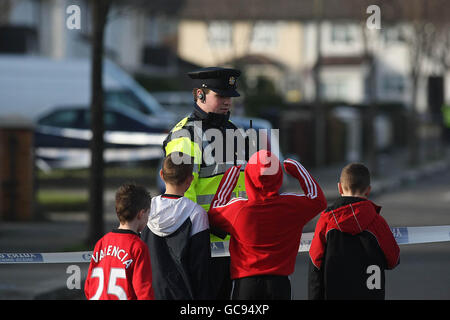 Kinder sprechen mit einem garda, der eine Kordon umarmt, an der Stelle, an der gestern Abend um 22.20 Uhr in Coolock, Dublin, ein Mann bei einem Gundland-ähnlichen Schusswaffenangriff getötet wurde. Die Schießerei auf der Ferrycarrig Road in Priorswood ist der vierte Todesfall von 2010 Waffen, nachdem letzte Woche drei Männer bei zwei separaten Angriffen in der Hauptstadt getötet wurden. Stockfoto