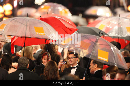 Gäste, die bei den Orange British Academy Film Awards im Royal Opera House in London ankommen, können sich unter Sonnenschirmen schützen. Stockfoto