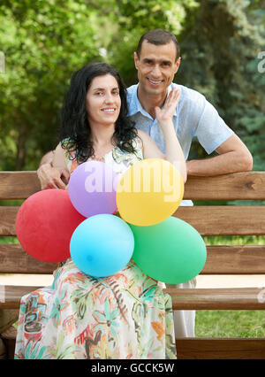 Romantisches Brautpaar mit Ballon sitzen auf Bank im Stadtpark und posiert, Sommersaison, Erwachsene Personen Mann und Frau Stockfoto