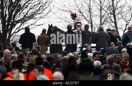 Rennfahrer beobachten die Umsiedlungssparaden vor dem Neptune Investments Management Hürdenlauf am zweiten Tag des Cheltenham Festivals 2010 auf der Cheltenham Rennbahn. Stockfoto