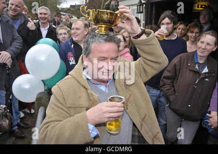 Nigel Twiston-Davies, Trainer des Cheltenham Gold Cup 2010 Sieger Imperial Commander genießt einen Drink, während er den Cup auf seinem Kopf während der Siegesparade vor dem Hollow Bottom Pub in Guiting Power, in der Nähe von Cheltenham balanciert. Stockfoto