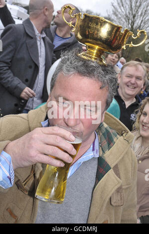 Nigel Twiston-Davies, Trainer des Cheltenham Gold Cup 2010 Sieger Imperial Commander genießt einen Drink, während er den Cup auf seinem Kopf während der Siegesparade vor dem Hollow Bottom Pub in Guiting Power, in der Nähe von Cheltenham balanciert. Stockfoto